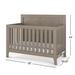 The Child Craft Kieran 4-in-1 Convertible Crib in Crescent Gray features a herringbone-patterned back panel, slatted sides, and includes a crib mattress. Dimensions: 44" H x 55" W x 29.25" D.