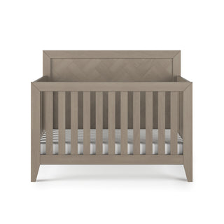 The Child Craft Kieran 4-in-1 Convertible Crib in Crescent Gray features vertical slats, a solid headboard, and comes with a striped mattress, shown against a white background.