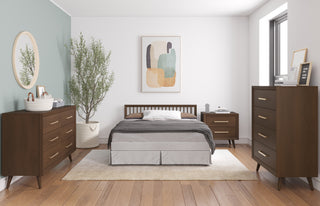 A modern bedroom with wooden furniture, a bed in the center, abstract art above it, a potted plant on the left, Child Craft Cranbrook Double Dresser in Toasted Chestnut and nightstands on each side, plus a window on the right letting in natural light.