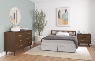 A modern bedroom with a wooden bed, Child Craft Cranbrook Double Dresser in Toasted Chestnut, matching nightstand, large potted plant, abstract wall art, round mirror, soft neutral colors, white and pale green walls, and hardwood flooring.