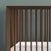 Close-up of the Child Craft Cranbrook 4-in-1 Convertible Crib in Toasted Chestnut, featuring vertical wooden slats and a white mattress against a muted green wall—perfect nursery furniture for a stylish space.