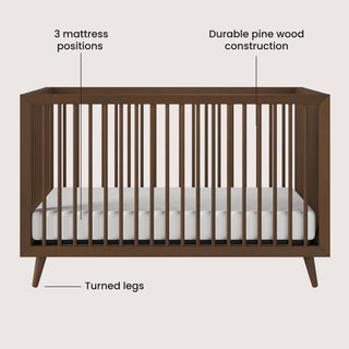 The Child Craft Cranbrook 4-in-1 Convertible Crib in Toasted Chestnut features durable pine wood construction, mid-century modern design with turned legs, a white mattress, and offers 3 adjustable mattress positions—ideal for a stylish nursery.