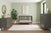 A modern nursery with sage green walls features the Child Craft Cranbrook 4-in-1 Convertible Crib in Lunar Gray, a matching dresser and chest, a large plant in a woven basket, a round mirror, abstract art above the crib, and a light rug on wood floors.