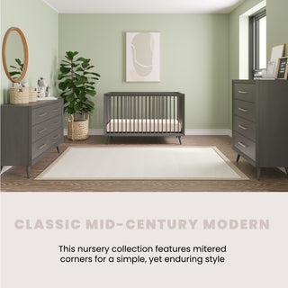 A nursery with sage green walls, dark wood crib, Child Craft Cranbrook Double Dresser in Lunar Gray, matching chest, round mirror, potted plant, abstract wall art, and light rug. Text: Classic Mid-Century Modern featuring timeless nursery furniture.