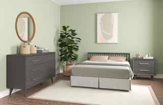 A modern bedroom with sage green walls, gray bed and furniture, a Child Craft Cranbrook Double Dresser in Lunar Gray with a round mirror, potted plant, abstract wall art, hardwood floors, and a light area rug.