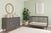 Modern nursery with sage green walls, the Child Craft Cranbrook 4-in-1 Convertible Crib in Lunar Gray, matching gray dresser, round mirror, potted plant, abstract wall art, woven baskets, sleek furniture, and wooden floors for a cozy minimalist feel.