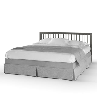 The Child Craft Cranbrook 4-in-1 Convertible Crib in Lunar Gray features a modern slatted headboard, white bedding, two pillows, and a light gray skirt—an elegant addition to any nursery, shown against a plain white background.