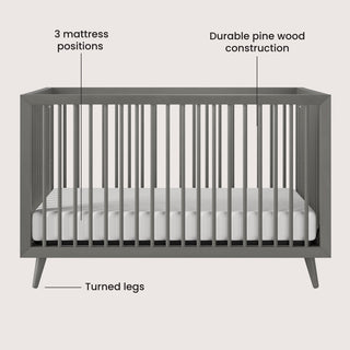 The Child Craft Cranbrook 4-in-1 Convertible Crib in Lunar Gray features vertical slats, turned legs, three mattress height options, and sturdy pine wood. Includes a white mattress and labels highlighting key features.