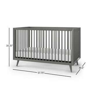 The Child Craft Cranbrook 4-in-1 Convertible Crib in Lunar Gray features a mid-century modern design with vertical slats and angled legs. Dimensions: 35.25"H x 57.75"W x 30.5"D. Comes with a white mattress inside the crib.