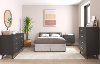 A modern bedroom with a black bed, two black dressers, a black nightstand, large potted plant, round mirror, abstract wall art, and a light rug on wood floors features the Child Craft Cranbrook 4-in-1 Convertible Crib in Ebony blending seamlessly into the space.