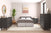 A modern bedroom with a black bed, two black dressers, a black nightstand, large potted plant, round mirror, abstract wall art, and a light rug on wood floors features the Child Craft Cranbrook 4-in-1 Convertible Crib in Ebony blending seamlessly into the space.