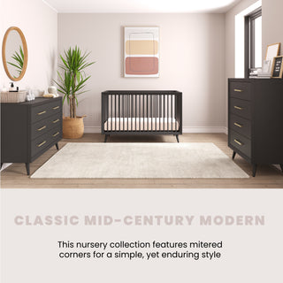 A stylish nursery features a black crib, Child Craft Cranbrook Double Dresser in Ebony, a round mirror, potted plant, framed wall art, and a light area rug, creating a cozy, mid-century modern vibe.