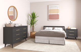 A modern bedroom featuring a gray bed, Child Craft Cranbrook Nightstand in Ebony, gray dresser, round mirror, large potted plant, abstract art on light beige walls, and light wood flooring with a beige rug.