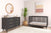 Modern nursery featuring the Child Craft Cranbrook 4-in-1 Convertible Crib in Ebony, matching dresser, round wall mirror, abstract art, woven basket with plant, plush toy, baby essentials, and a neutral rug on wood floors.