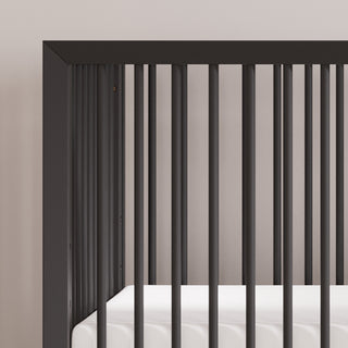 Close-up of the Child Craft Cranbrook 4-in-1 Convertible Crib in Ebony, featuring modern vertical slats and a white mattress. This stylish, functional nursery piece stands against a light wall, blending seamlessly with any décor.