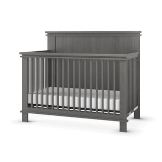 The Child Craft Denman 4-in-1 Convertible Crib in Midnight Gray features a tall, solid headboard and vertical slats with a white mattress, showcasing a simple modern design against a white background.