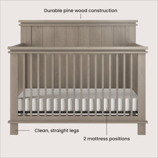 Front view of the Child Craft Denman 4-in-1 Convertible Crib in Crescent Gray, featuring durable pine wood, clean straight legs, and 2 mattress positions. A white mattress rests inside the crib with vertical slats.