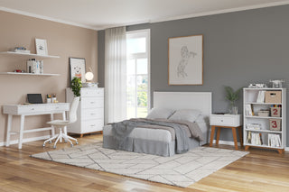 A modern bedroom featuring the Child Craft Soho 4 Drawer Chest in White/Natural, a bed, gray and beige walls, a desk with chair, white shelves, bookshelf, nightstand, and a large window with sheer curtains letting in daylight.