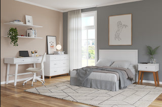 A modern bedroom features a gray accent wall, neatly made bed, white desk and chair, dresser, wall art, and the Child Craft Soho Nightstand in White/Natural. Sunlight from a large window with sheer curtains brightens the cozy, organized space.