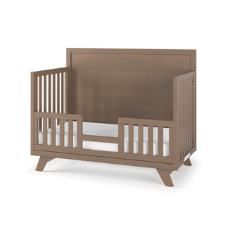 The Child Craft Toddler Guard Rail in Dusty Heather features a high backboard, side rails with vertical slats, a low guard rail at the front, a white mattress, and light brown baby-safe finishes for safety and style.
