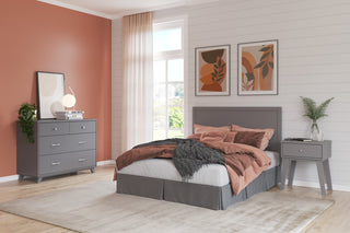 A modern bedroom showcases a gray bed, salmon pink bedding, and sleek nursery furniture including the Child Craft Soho 4-in-1 Flat Top Convertible Crib in Cool Gray. Two abstract art prints hang above the bed, with a beige rug on the wooden floor by a sunlit window.