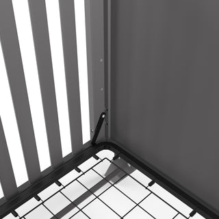 Close-up of the Soho 4-in-1 Flat Top Convertible Crib by Child Craft in Cool Gray, showcasing its vertical slats, mesh mattress support with bracket, and matte frame—an elegant, stylish choice for modern nurseries.