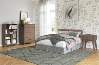 A cozy, modern bedroom with leafy wallpaper, a wooden bed dressed in green and pink bedding, a nightstand, Child Craft Soho 4 Drawer Chest in Dusty Heather, bookshelf, geometric green rug, and a large window filling the space with natural light.