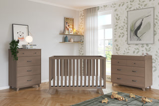 A nursery with a wooden crib, dresser, and the Child Craft Soho 4 Drawer Chest in Dusty Heather. Toys rest on a green rug, artwork and decor fill the shelves, and sunlight streams in beside leafy wallpaper on one wall.