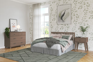 A bright bedroom featuring a bed with patterned bedding, leafy wallpaper, framed art, a geometric rug on wood floors, and the Child Craft Soho Nightstand in Dusty Heather beside a dresser with decor under a large window.
