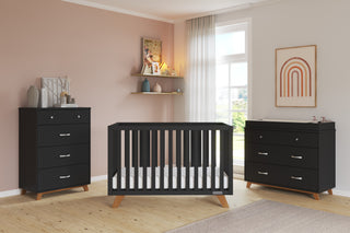 Modern nursery with blush pink walls, the Child Craft Soho 4-in-1 Convertible Crib in Ebony, matching black dresser and changing table, sheer-curtained window, wall art, decorative shelf, and a light rug on wooden floors.