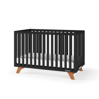 The Child Craft Soho 4-in-1 Convertible Crib in Ebony features wooden angled legs, vertical slats on all sides, and a white mattress. It converts into a toddler bed and is shown against a plain white background.