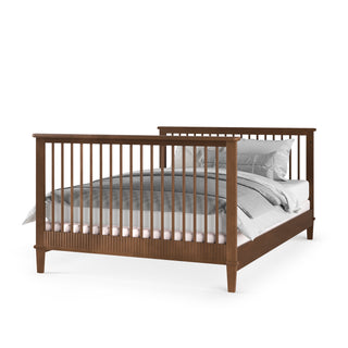 The Child Craft F06401 Full-Size Bed Rails in Cocoa Bean are shown supporting a wooden bed with vertical slats on the headboard and footboard, dressed in white and gray bedding against a plain white background.