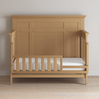The Child Craft F09554 Toddler Guard Rail in Biscotti adds a partial crib guard rail to your toddler bed—perfect for converting your Child Craft crib for safe sleeping. Shown with a high back panel and white mattress on a light wood floor.
