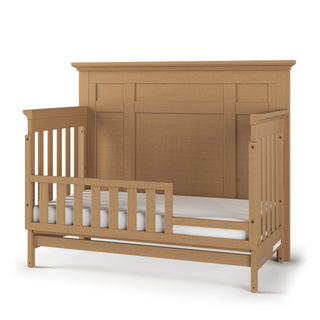 The Child Craft F09554 Toddler Guard Rail in Biscotti features crib-style side rails and a high paneled headboard for easy toddler bed conversion, shown with a white mattress.