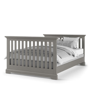 The Child Craft F06434 Full-Size Bed Rail in Lunar Grey features a wooden frame with vertical slats on the headboard and footboard, neatly dressed in white and gray bedding and pillows.