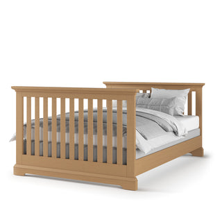 The Child Craft F06434 Full-Size Bed Rails in Biscotti are displayed with vertical slats on the headboard and footboard, sturdy rails, and white and gray bedding and pillows, set against a white background.
