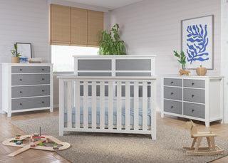 A modern nursery features Child Craft's Ocean Grove Double Dresser in white/gray, complemented by a rocking horse, wooden train toys on a rug, a potted plant, abstract blue wall art, wood flooring, and nautical farmhouse accents.