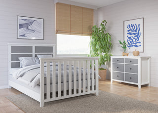 A modern bedroom with Child Craft Full-Size Bed Rails in white/gray, gray bedding, a wood dresser, abstract art, a green potted plant, and natural light filtering through bamboo blinds.