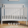 The Child Craft Scout 4-in-1 Convertible Crib in Matte White features vertical slats, a beadboard headboard with an arched detail, and versatile use—an ideal nursery piece shown against a blue paneled wall and wood floor.