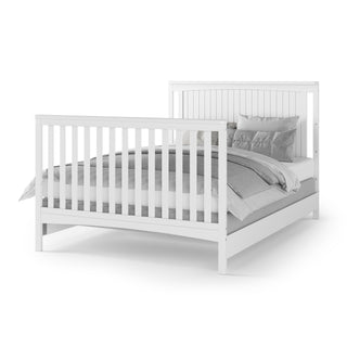 The Child Craft Scout 4-in-1 Convertible Crib in Matte White features a slatted headboard and footboard, dressed in gray and white bedding with multiple gray pillows—an ideal blend of style and function for any baby nursery.