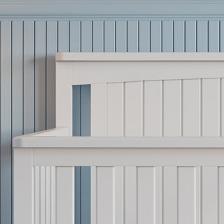 Close-up of the Child Craft Scout 4-in-1 Convertible Crib in Matte White with vertical slats, set against a light blue paneled wall for a calm, minimalistic nursery vibe.