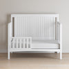 The Child Craft Scout 4-in-1 Convertible Crib in Matte White features a partial safety rail and wooden slat paneling, making it a minimalist nursery piece that pairs well with light walls and wooden floors.