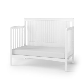 The Child Craft Scout 4-in-1 Convertible Crib in Matte White features vertical slats, a solid grooved back panel, and a plain white mattress—ideal for any nursery. Shown on a white background.
