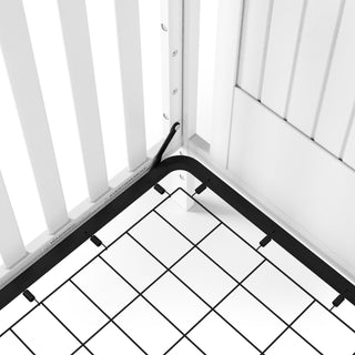 A close-up of the Child Craft Scout 4-in-1 Convertible Crib in Matte White, showing its black metal spring base against paneled white walls in a modern nursery.