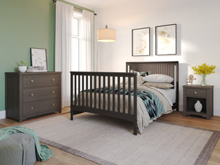 A stylish baby nursery featuring the Child Craft Scout 4-in-1 Convertible Crib in Dapper Gray, matching dresser and nightstand, green accent wall, framed art, beige rug, hanging lamp, and a window with white curtains for natural light.