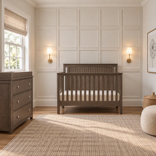 A gray Child Craft Scout 4-in-1 Convertible Crib with a beadboard headboard sits in a nursery next to a matching three-drawer changing table.