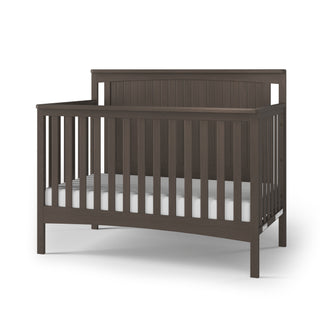 The Child Craft Scout 4-in-1 Convertible Crib in Dapper Gray features vertical slats on all sides and includes a white mattress, making it a versatile nursery furniture piece, shown against a plain white background.