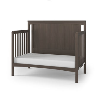 The Child Craft Scout 4-in-1 Convertible Crib in Dapper Gray features vertical side slats, a solid back panel, and a white mattress, displayed on a plain white background—ideal modern nursery furniture.
