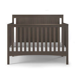 The Child Craft Scout 4-in-1 Convertible Crib in Dapper Gray features vertical slats on all sides, a solid beadboard headboard, and comes with a white mattress and adjustable mattress support, shown on a white background.