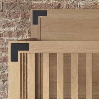 Close-up of the Child Craft Lucas 4-in-1 Convertible Crib in Nutmeg, featuring light wood with black metal brackets, vertical slats, and a modern minimalist design, set against a rustic brick wall.